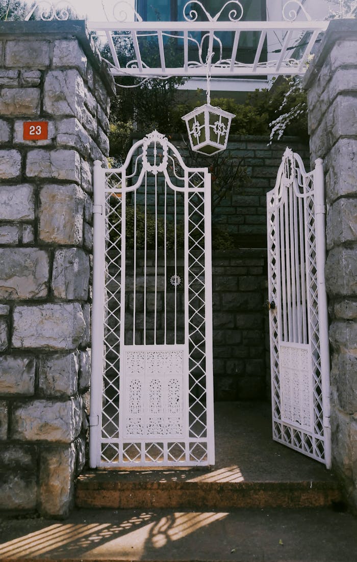 Charming white wrought iron gate set in a stone entrance with lush greenery in the background.